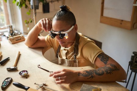 Foto de Retrato de joyero artesanal con tatuajes trabajando en obra de arte en mesa de madera - Imagen libre de derechos