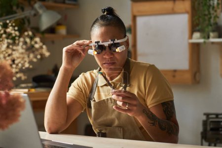 Photo for Portrait of artisanal jeweler wearing magnifying glasses while working on art piece - Royalty Free Image