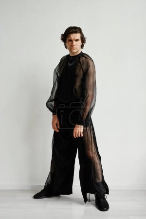 Photo for Full length portrait of non binary man wearing black chiffon outfit posing against white in fashion studio - Royalty Free Image