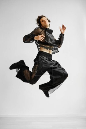 Foto de Acción tiro de hombre no binario con traje de encaje saltando en el aire contra blanco - Imagen libre de derechos