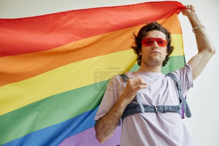 Foto de Cintura hacia arriba retrato de un joven gay ondeando la bandera del orgullo vistiendo un traje colorido, espacio para copiar - Imagen libre de derechos
