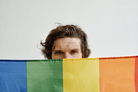Photo for Minimal concept shot of young gay man holding pride flag, eyes visible looking at camera - Royalty Free Image