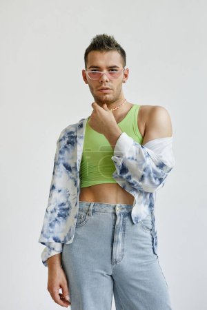 Téléchargez les photos : Portrait vertical de jeune homme gay portant une tenue extravagante avec haut de culture contre blanc en studio de mode - en image libre de droit