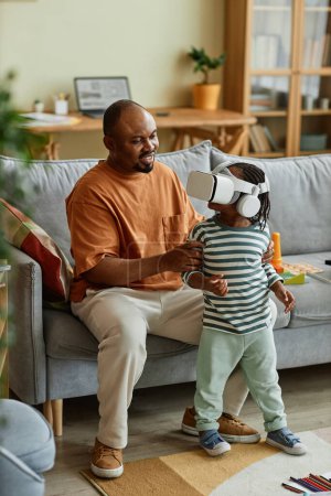 Photo for Vertical portrait of cute black child wearing VR headset and enjoying virtual reality entertainment with father supporting - Royalty Free Image