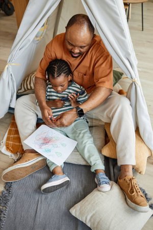 Téléchargez les photos : Portrait vertical pleine longueur d'un père noir aimant avec un enfant rassemblé dans une tente de jeu - en image libre de droit