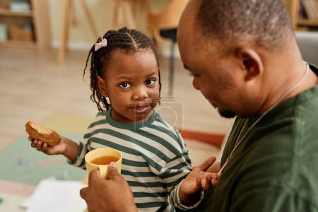 Foto de Alto ángulo retrato de linda chica negra compartiendo cookies con el padre y mirando a la cámara - Imagen libre de derechos