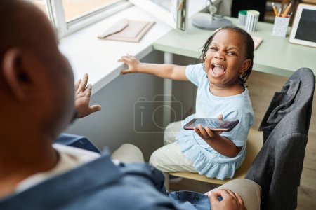 Photo for High angle portrait of black little girl screaming at father trying to take away smartphone - Royalty Free Image