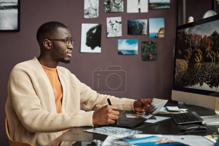 Foto de Hombre negro creativo edición de fotos de paisaje en el ordenador cuando se trabaja desde casa - Imagen libre de derechos