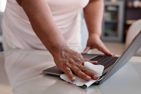 Téléchargez les photos : Gros plan de femme noire méconnaissable nettoyage ordinateur portable avec lingettes désinfectantes, espace de copie - en image libre de droit