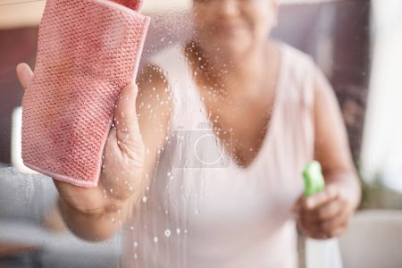 Photo for Close up background image of senior woman cleaning glass windows focus on hand holding wipe, copy space - Royalty Free Image