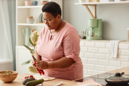 Foto de Retrato de cintura hacia arriba de la mujer negra de alto nivel cocinando ensalada saludable en la acogedora cocina casera, espacio para copiar - Imagen libre de derechos