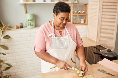 Photo for High angle portrait of black senior woman cutting vegetables in cozy kitchen, warm tones - Royalty Free Image