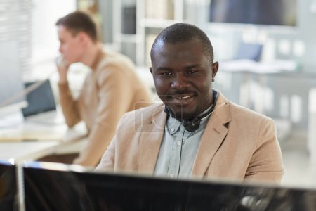 Photo for Portrait of smiling black man looking at computer screen while working in customer support and surveillance center - Royalty Free Image