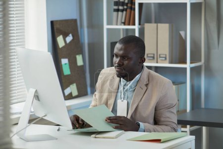 Téléchargez les photos : Portrait d'un homme d'affaires noir utilisant un ordinateur de bureau au bureau et travaillant avec des documents - en image libre de droit
