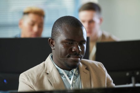 Foto de Retrato del hombre negro sonriente mirando la pantalla de la computadora mientras trabaja en la oficina de soporte técnico - Imagen libre de derechos