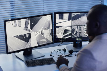 Foto de Vista trasera hombre negro mirando imágenes de cámaras de vigilancia en el centro de seguridad, tonos azules - Imagen libre de derechos