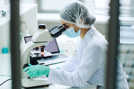 Photo for Side view portrait of young female technician looking in microscope while working in medical lab - Royalty Free Image