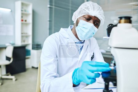 Téléchargez les photos : Portrait de l'homme noir concentré portant un masque facial tout en faisant de la recherche dans un laboratoire médical - en image libre de droit