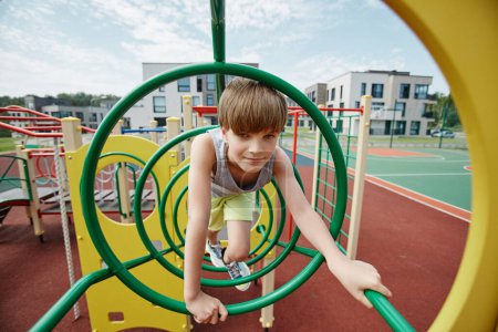 Téléchargez les photos : Portrait de garçon jouant dans la salle de gym jungle sur aire de jeux colorée et regardant la caméra, l'espace de copie - en image libre de droit