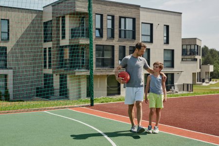 Téléchargez les photos : Portrait complet de père et fils jouant au basket ensemble et debout sur le terrain dans un complexe d'habitation moderne, espace de copie - en image libre de droit