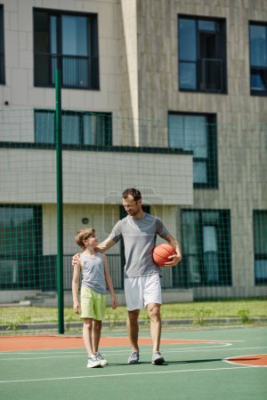 Photo for Vertical full length portrait of father and son playing basketball together and standing on court in sunlight - Royalty Free Image