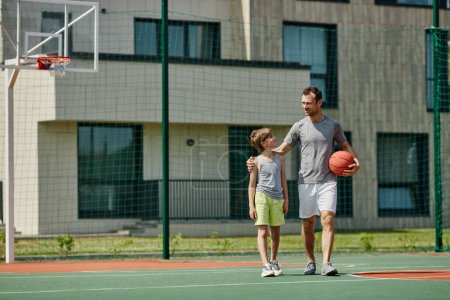 Foto de Retrato de larga duración de feliz padre e hijo jugando baloncesto juntos y de pie en la cancha a la luz del sol, espacio de copia - Imagen libre de derechos