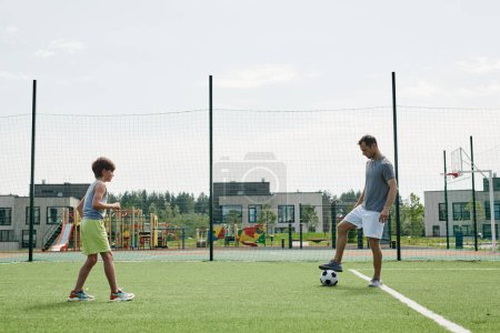 Photo for Side view of father and son playing football together in outdoor court at modern housing complex - Royalty Free Image