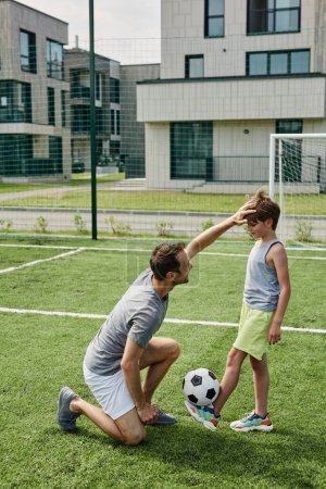 Téléchargez les photos : Portrait vertical de père et fils aimants jouant au football ensemble à la cour extérieure - en image libre de droit