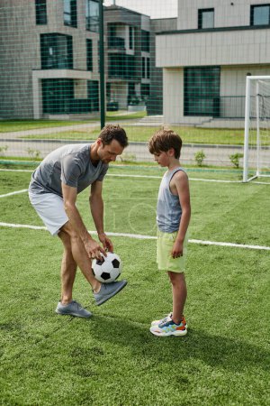 Photo for Vertical side view portrait of loving father teaching son football in outdoor court - Royalty Free Image
