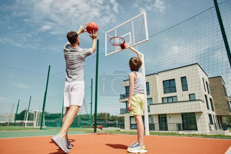 Foto de Retrato de gran angular de padre e hijo jugando baloncesto juntos, hombre disparando pelota a través del aro - Imagen libre de derechos