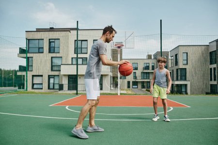 Téléchargez les photos : Portrait complet du père et du fils jouant au basket-ball ensemble à l'extérieur par un complexe d'habitation moderne - en image libre de droit