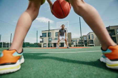 Téléchargez les photos : Père et fils jouant au basket-ball tiré à travers les jambes des garçons défendant la balle, copier l'espace - en image libre de droit