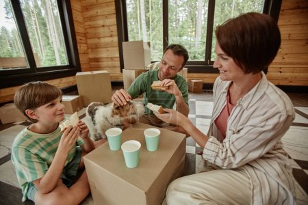 Photo for Happy family moving into new house and enjoying lunch with makeshift table, copy space - Royalty Free Image