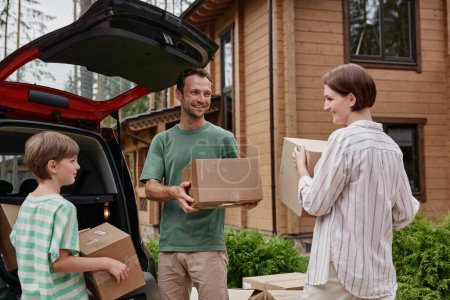 Photo for Portrait of happy family unloading boxes from car trunk while moving into new house in nature - Royalty Free Image