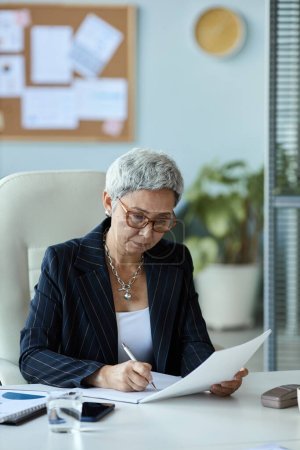 Foto de Retrato vertical de la mujer mayor como jefa mujer leyendo documento en el lugar de trabajo en la oficina - Imagen libre de derechos