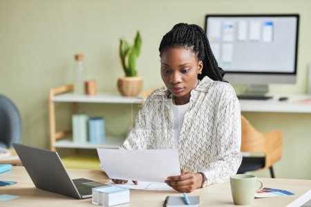 Téléchargez les photos : Portrait minimal de la jeune femme noire utilisant un ordinateur portable tout en travaillant au bureau dans un cadre de bureau, espace de copie - en image libre de droit