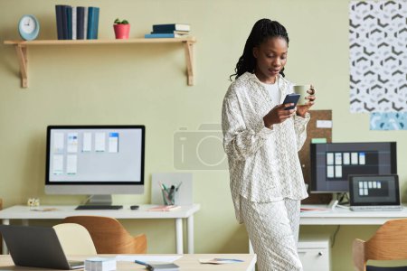 Foto de Retrato de una mujer negra moderna usando un teléfono inteligente mientras toma un descanso en un entorno de oficina mínimo, espacio para copiar - Imagen libre de derechos