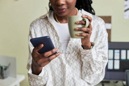 Téléchargez les photos : Gros plan de la jeune femme noire en utilisant un smartphone et profiter du café tout en prenant une pause du travail, copier l'espace - en image libre de droit