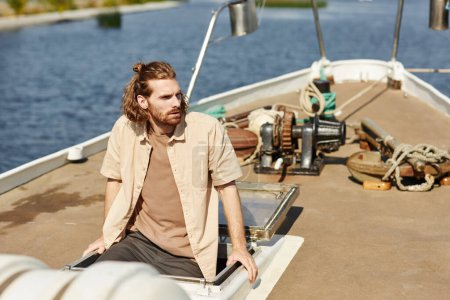 Photo for Portrait of bearded young man sailing on boat and looking away lit by sunlight, copy space - Royalty Free Image