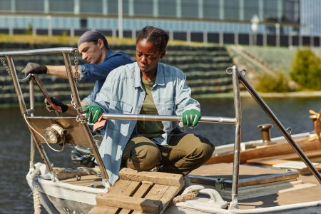 Téléchargez les photos : Portrait complet de jeune femme noire travaillant sur un bateau éclairé par la lumière du soleil, espace de copie - en image libre de droit