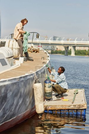 Photo for Vertical portrait of two sailors, man and woman working on boat in docks lit by sunlight - Royalty Free Image