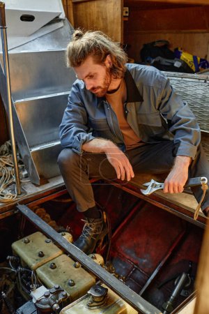 Photo for Vertical side view portrait of bearded young man repairing boat engine - Royalty Free Image