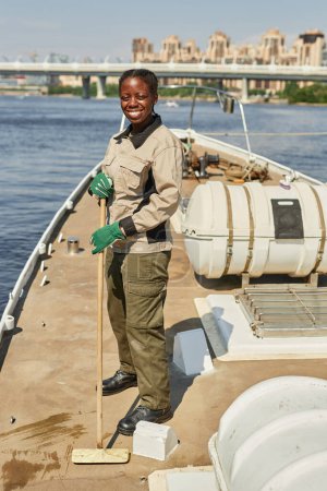Téléchargez les photos : Portrait vertical de femmes souriantes qui nettoient les planchers sur un bateau ou un yacht à la lumière du soleil et regardent la caméra - en image libre de droit