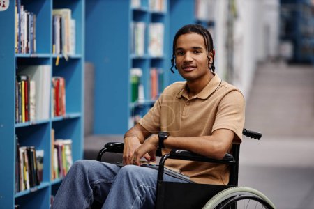 Foto de Retrato del joven negro con discapacidad en el entorno de la biblioteca en la universidad moderna sonriendo a la cámara - Imagen libre de derechos