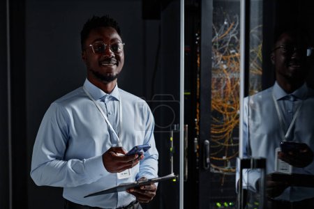 Photo for Waist up portrait of smiling black man as network engineer standing by server cabinet in data center and looking at camera, copy space - Royalty Free Image