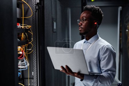 Photo for Waist up portrait of black man as network engineer in server room using laptop, minimal - Royalty Free Image