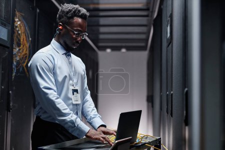 Photo for Backlit side view portrait of data engineer wearing formal uniform while using laptop in server room - Royalty Free Image