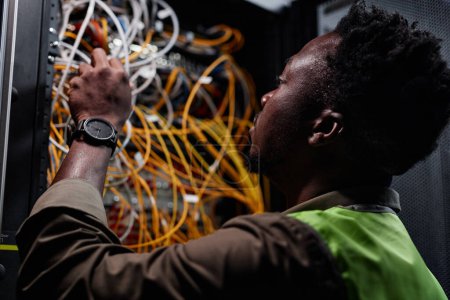 Photo for Close up of black man as network technician connecting cables and wires while repairing server in data center - Royalty Free Image