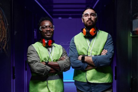 Photo for Waist up portrait of two technicians standing in server room with arms crossed and looking at camera lit by neon light - Royalty Free Image