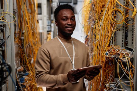 Photo for Waist up portrait of black man as system administrator standing in server room and smiling at camera - Royalty Free Image